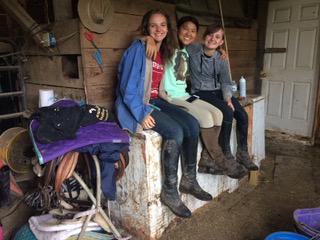 Three girls with arms around each other sitting on tack box.