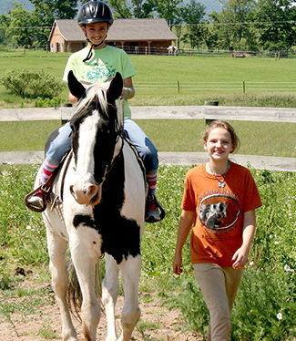 Girl riding horse with instructor walking beside.